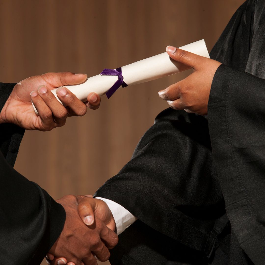 A diploma is handed from one individual to another as they shake hands