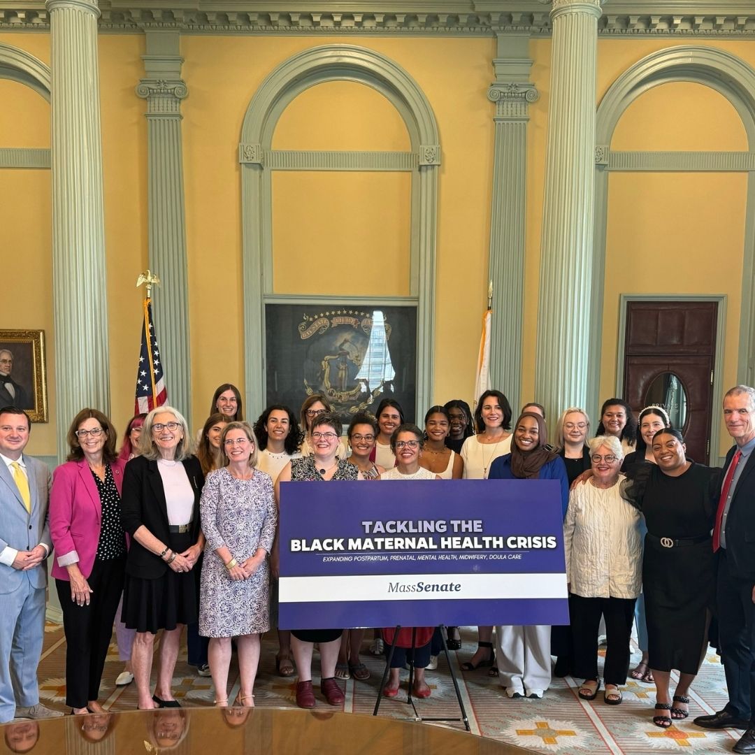 Many gathered around a sign that says "TACKLING THE BLACK MATERNAL HEALTH CRISIS"